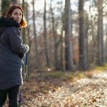 Frau auf einem Waldweg, im Hintergrund, etwas weiter entfernt der Hund.