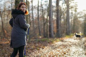 Frau auf einem Waldweg, im Hintergrund, etwas weiter entfernt der Hund.
