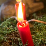 Zwei Kerzen eines Adventsgestecks auf Moos. Im Hintergrund ist eine Holzfigur zu sehen.