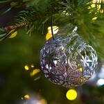 Eine Weihnachtskugel aus Silberblech die an einem Zweig hängt.